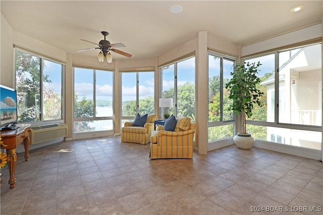 unfurnished sunroom featuring a wall mounted air conditioner, plenty of natural light, ceiling fan, and a water view