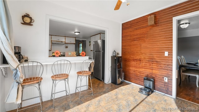 kitchen featuring stainless steel fridge, kitchen peninsula, wood walls, and white cabinetry