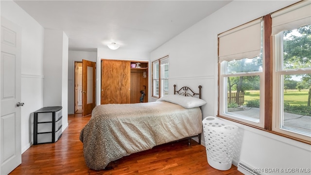 bedroom with multiple windows, baseboard heating, and hardwood / wood-style flooring