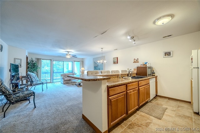 kitchen featuring hanging light fixtures, ceiling fan with notable chandelier, kitchen peninsula, sink, and light colored carpet