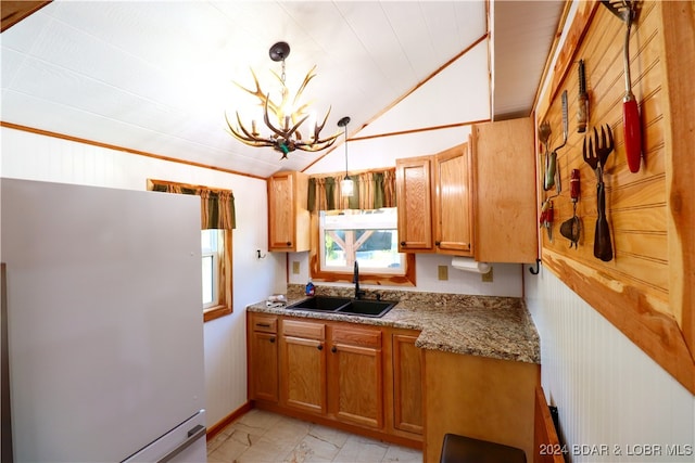 kitchen featuring sink, white refrigerator, a chandelier, pendant lighting, and vaulted ceiling