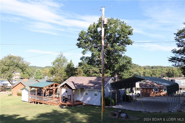 rear view of property featuring a carport, a wooden deck, and a lawn