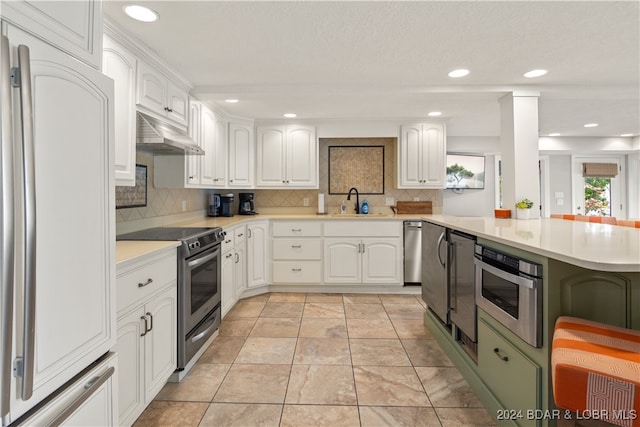 kitchen with kitchen peninsula, sink, tasteful backsplash, white cabinetry, and appliances with stainless steel finishes