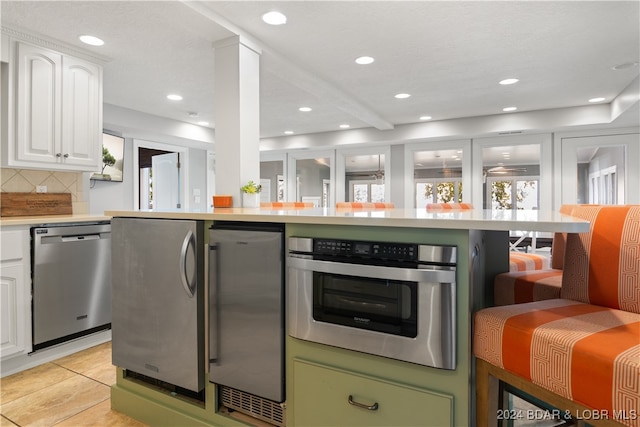 kitchen with stainless steel appliances, white cabinetry, light tile patterned flooring, and tasteful backsplash