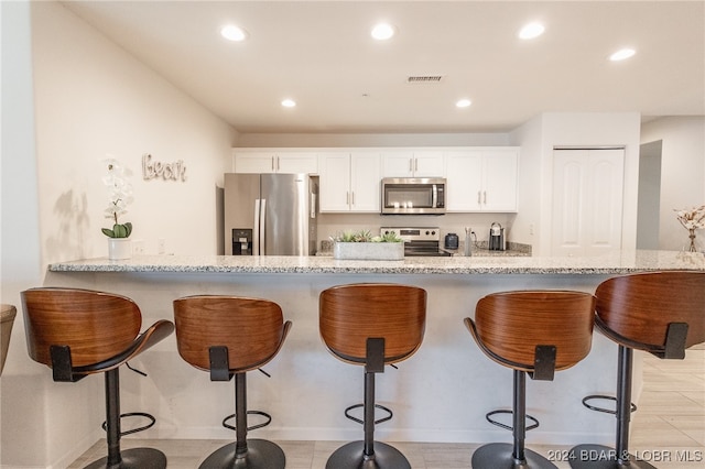 kitchen with a breakfast bar area, white cabinetry, kitchen peninsula, appliances with stainless steel finishes, and light stone countertops