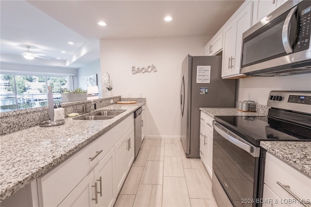 kitchen with appliances with stainless steel finishes, white cabinetry, light stone counters, ceiling fan, and sink