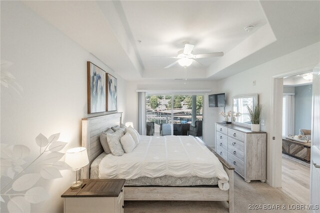 carpeted bedroom featuring ceiling fan, a tray ceiling, and access to exterior