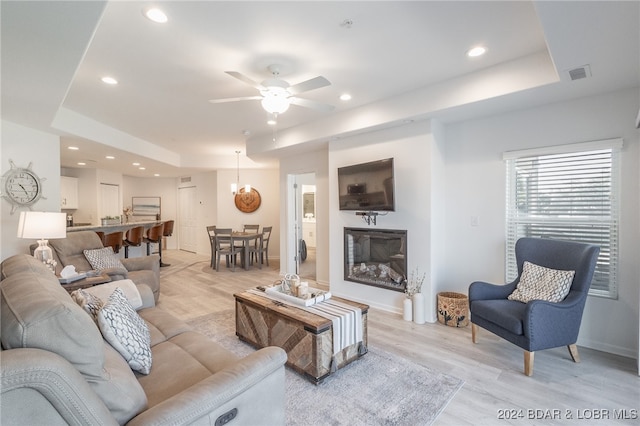 living room featuring light wood-type flooring, a raised ceiling, and ceiling fan