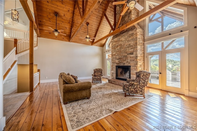 living room featuring hardwood / wood-style flooring, high vaulted ceiling, a stone fireplace, ceiling fan, and wooden ceiling