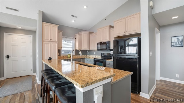 kitchen with lofted ceiling, black appliances, a center island, and light stone countertops