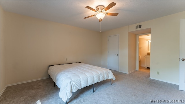 bedroom with ceiling fan, light colored carpet, and ensuite bath