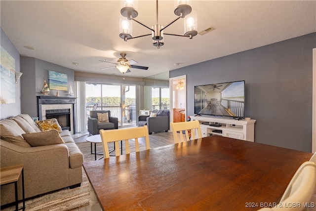 living room with a tile fireplace, ceiling fan with notable chandelier, and light wood-type flooring