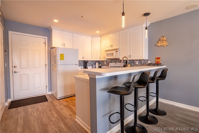 kitchen with white appliances, light wood-type flooring, kitchen peninsula, decorative light fixtures, and white cabinets