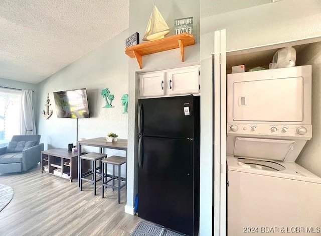 kitchen featuring black fridge, white cabinets, lofted ceiling, light hardwood / wood-style flooring, and stacked washer and dryer