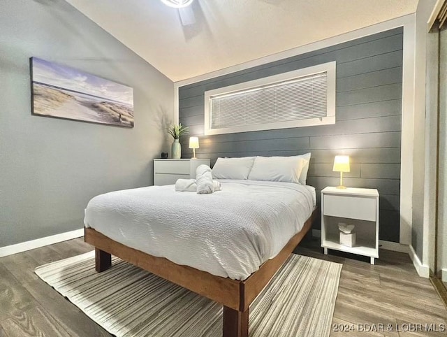 bedroom with lofted ceiling, wood walls, hardwood / wood-style floors, and ceiling fan