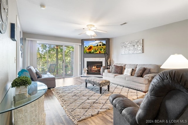 living room featuring light wood-type flooring, ceiling fan, and a high end fireplace