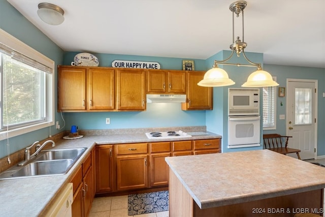 kitchen with light tile patterned flooring, white appliances, a kitchen island, decorative light fixtures, and sink