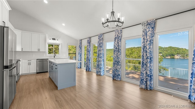 kitchen with white cabinets, a kitchen island, decorative light fixtures, appliances with stainless steel finishes, and light wood-type flooring