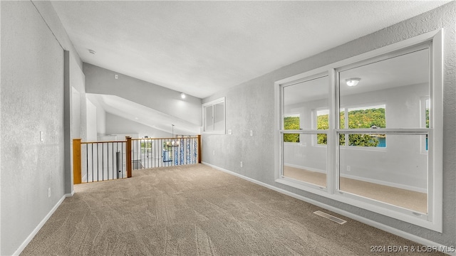 spare room with carpet, vaulted ceiling, and a textured ceiling