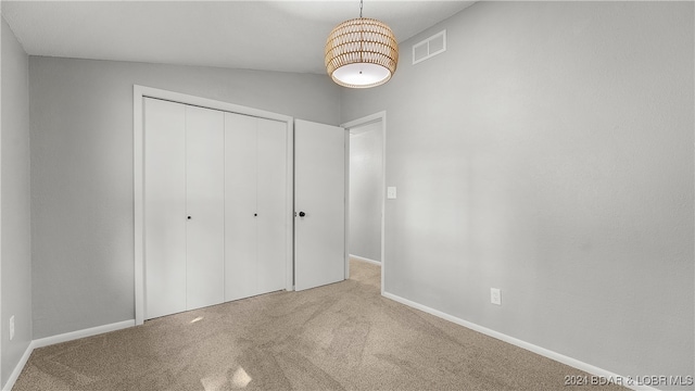 unfurnished bedroom with lofted ceiling, light colored carpet, and a closet