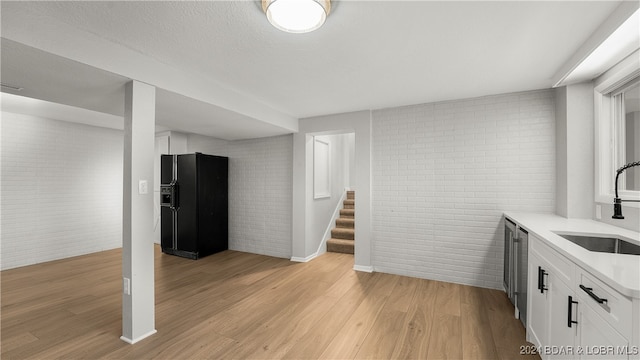 interior space with light hardwood / wood-style floors, black refrigerator with ice dispenser, sink, and brick wall