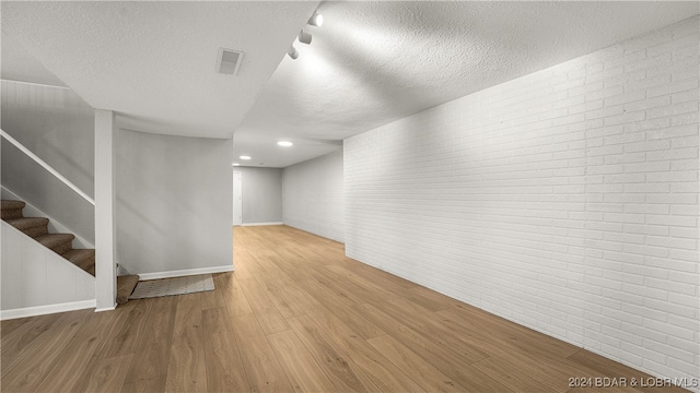 unfurnished room featuring light wood-type flooring, a textured ceiling, and brick wall