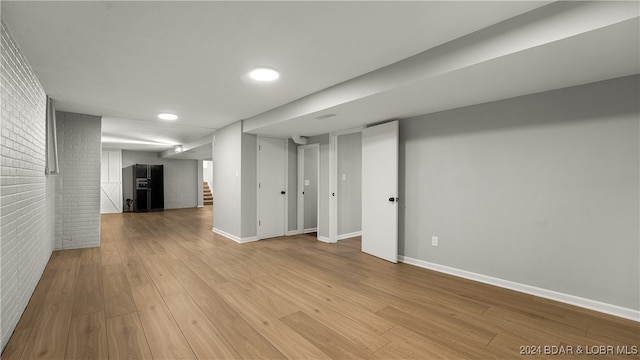 basement featuring light wood-type flooring and brick wall