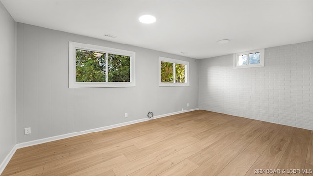 spare room with brick wall and light wood-type flooring