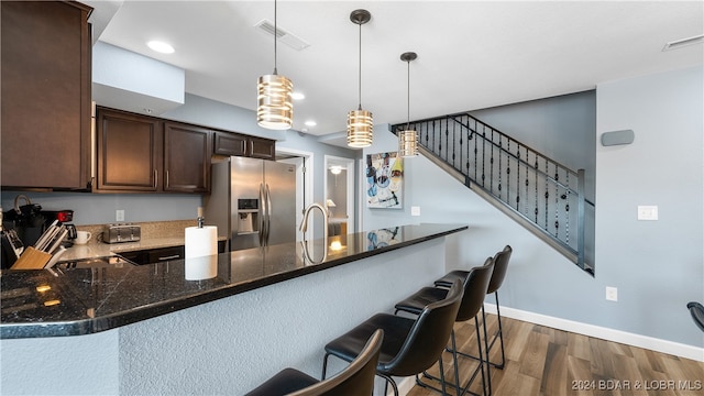 kitchen with pendant lighting, stainless steel fridge, kitchen peninsula, dark wood-type flooring, and a breakfast bar area