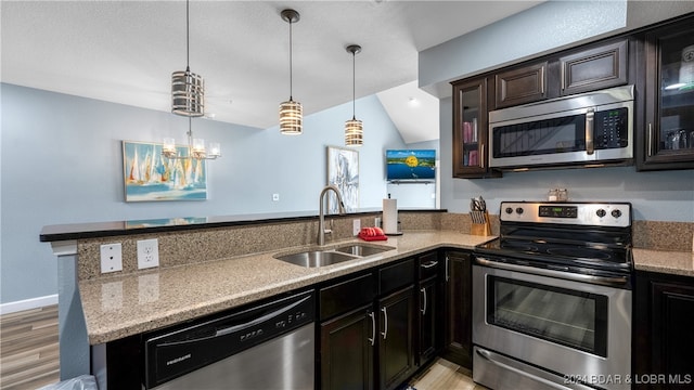 kitchen with vaulted ceiling, kitchen peninsula, stainless steel appliances, light wood-type flooring, and sink