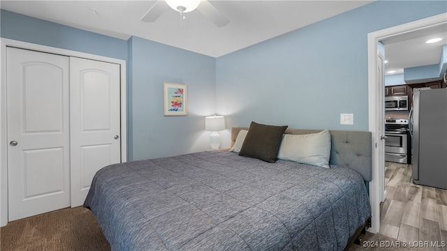 bedroom with light wood-type flooring, stainless steel refrigerator, ceiling fan, and a closet