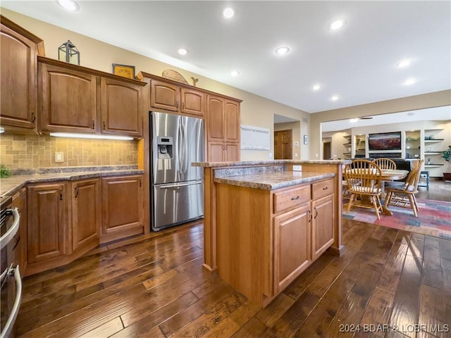 kitchen featuring a center island, dark hardwood / wood-style floors, stainless steel fridge, tasteful backsplash, and light stone counters