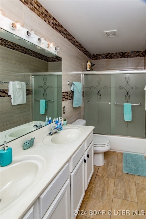 full bathroom with tile walls, combined bath / shower with glass door, vanity, and toilet