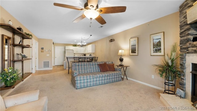 carpeted living room with a stone fireplace and ceiling fan with notable chandelier