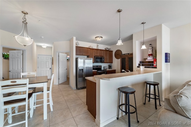 kitchen featuring kitchen peninsula, a kitchen bar, hanging light fixtures, appliances with stainless steel finishes, and light tile patterned floors