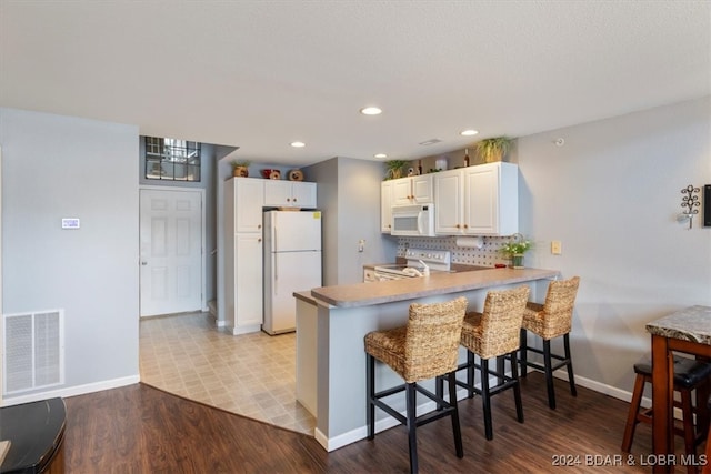 kitchen with light hardwood / wood-style floors, a breakfast bar area, white cabinets, kitchen peninsula, and white appliances