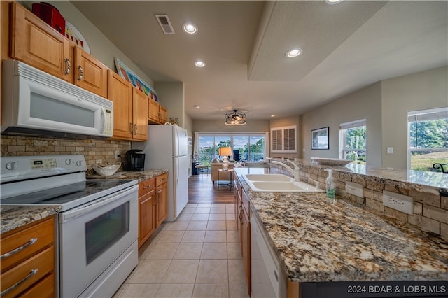 kitchen with light stone counters, light tile patterned floors, sink, white appliances, and a kitchen island with sink