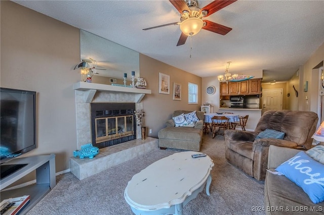 living room featuring a tile fireplace, ceiling fan with notable chandelier, light colored carpet, and a textured ceiling