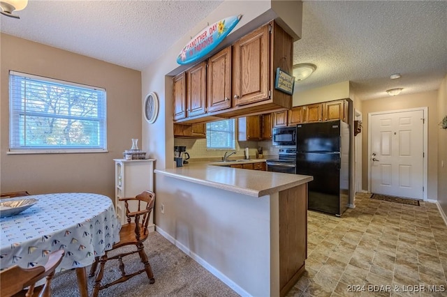 kitchen featuring kitchen peninsula, a textured ceiling, a breakfast bar, and black appliances