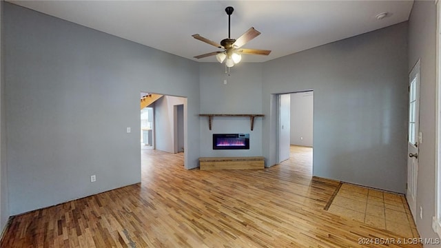 unfurnished living room featuring ceiling fan, a towering ceiling, and light hardwood / wood-style flooring