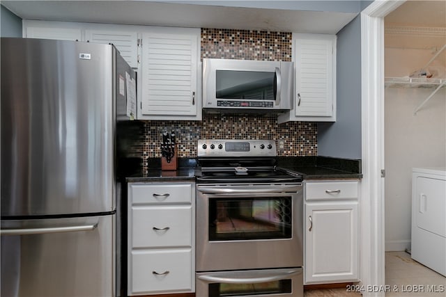 kitchen with decorative backsplash, washer / dryer, dark stone countertops, white cabinetry, and appliances with stainless steel finishes