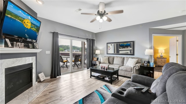 living room featuring a fireplace, ceiling fan, and light hardwood / wood-style flooring