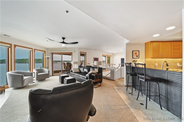 living room featuring ceiling fan, bar area, light tile patterned flooring, and a water view