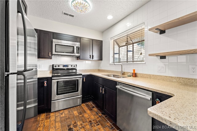 kitchen with sink, a textured ceiling, tasteful backsplash, light stone counters, and stainless steel appliances