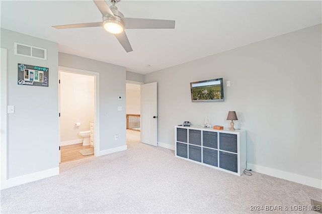 bedroom featuring light carpet, ensuite bathroom, and ceiling fan