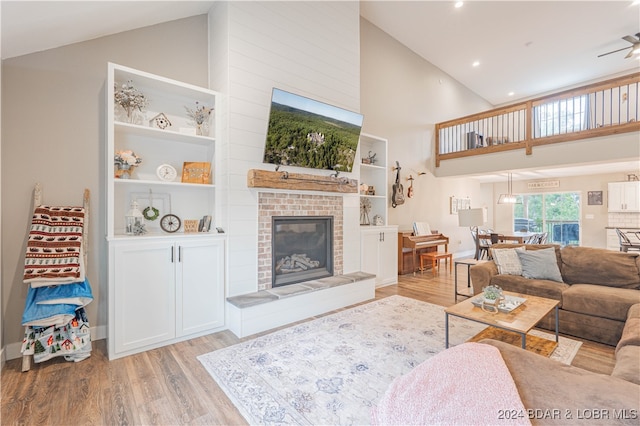 living room with ceiling fan, a fireplace, light hardwood / wood-style floors, and high vaulted ceiling