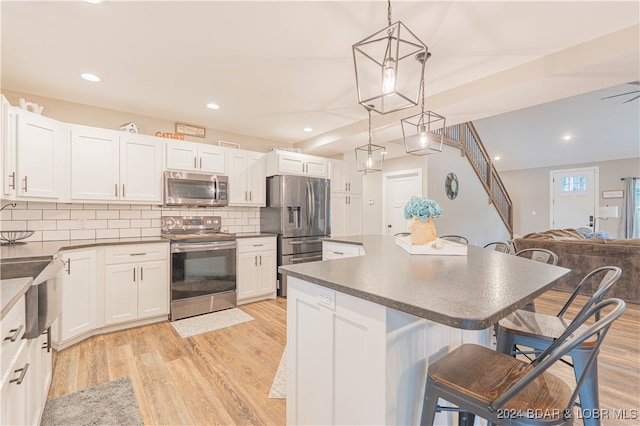 kitchen featuring stainless steel appliances, hanging light fixtures, a kitchen bar, and white cabinetry