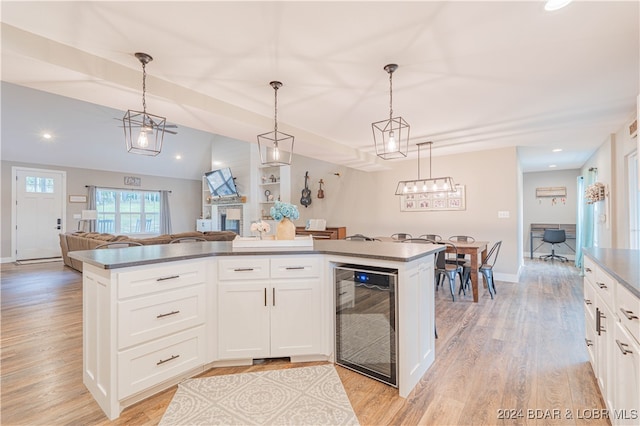 kitchen featuring white cabinets, pendant lighting, beverage cooler, light hardwood / wood-style flooring, and a center island