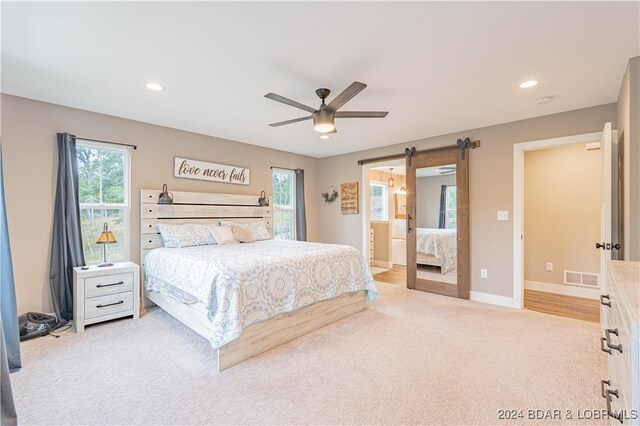 bedroom featuring ceiling fan, light colored carpet, ensuite bath, and a barn door