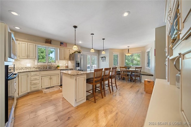 kitchen featuring pendant lighting, cream cabinets, a center island, stainless steel appliances, and light stone countertops